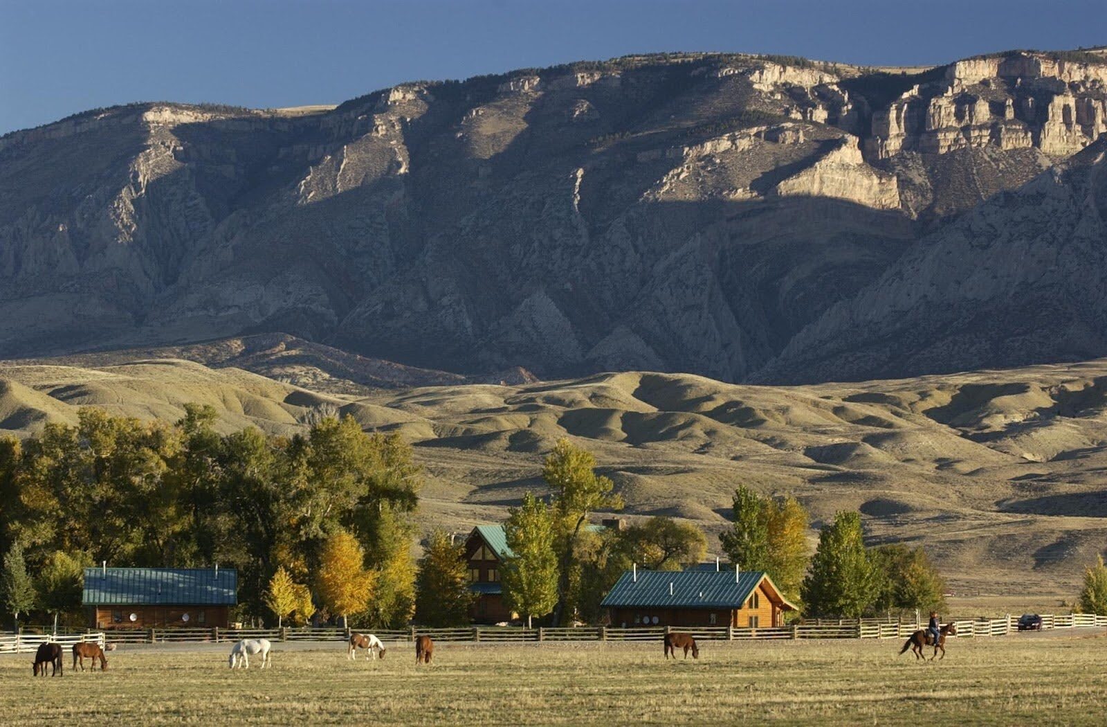 Ranch buildings and trees below a broad mountain ridge.