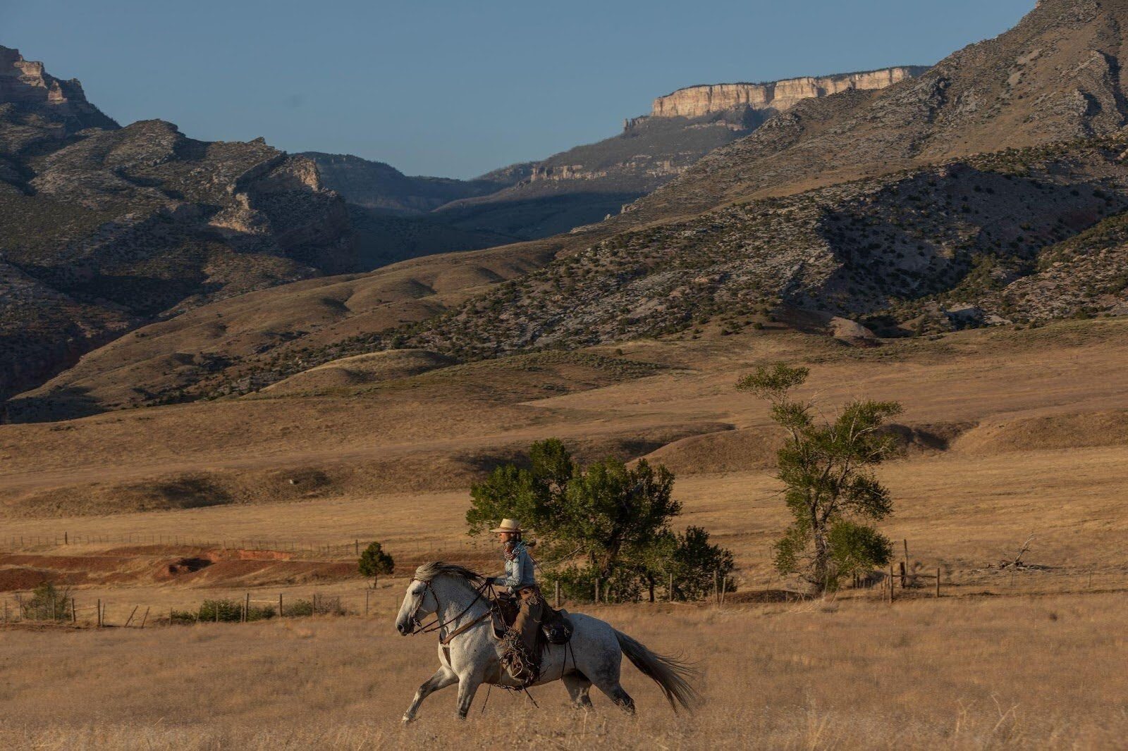 Horseback riders crossing open grassland with mountains behind.