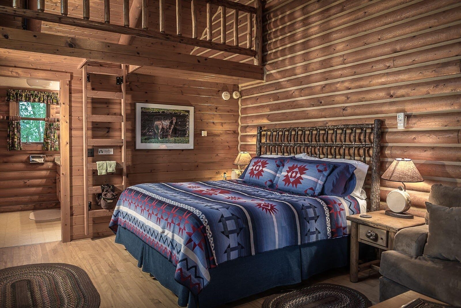 Bed with a patterned quilt inside a log-walled guest room.