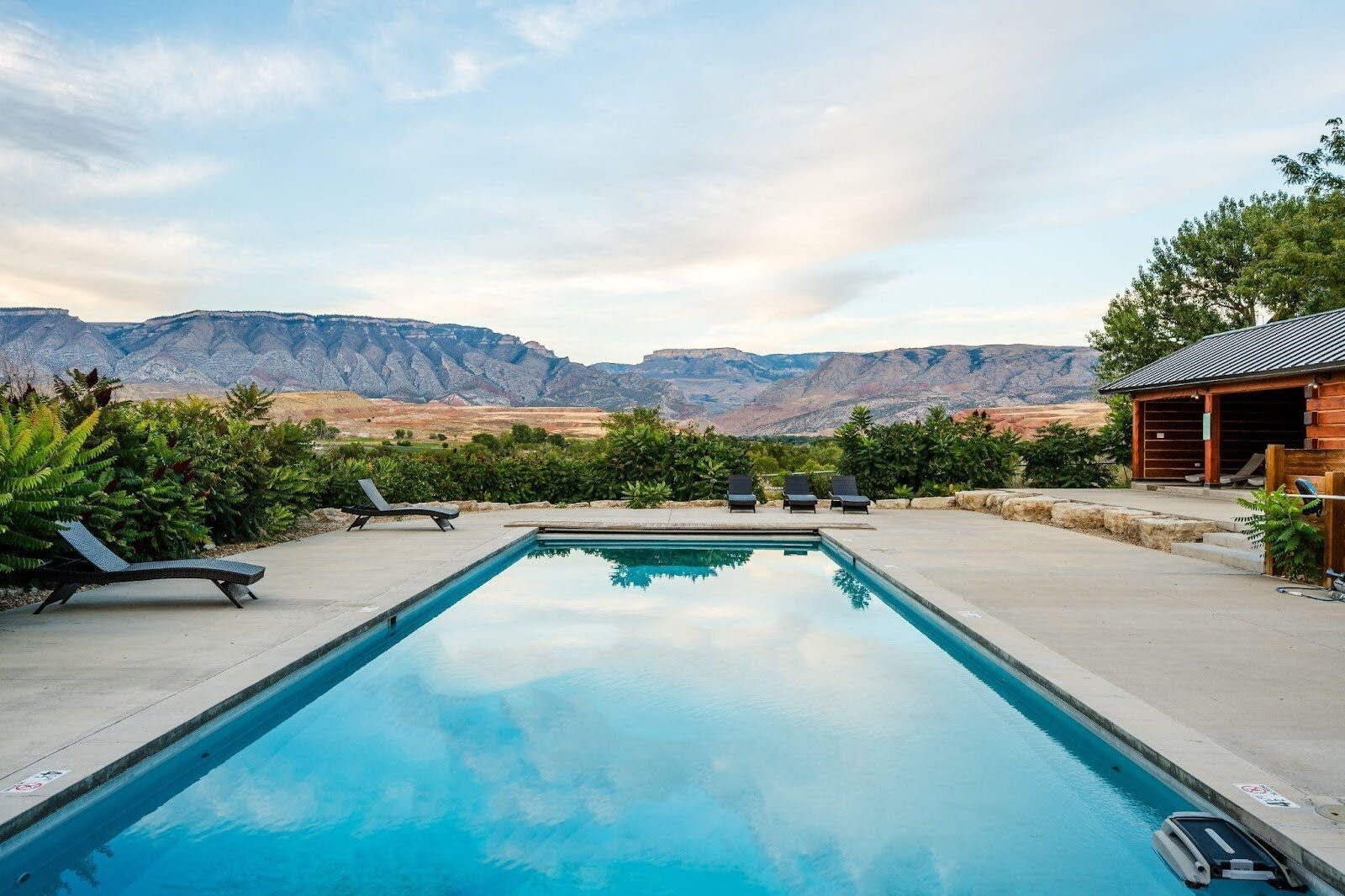 Outdoor swimming pool with ranch buildings and mountains beyond.