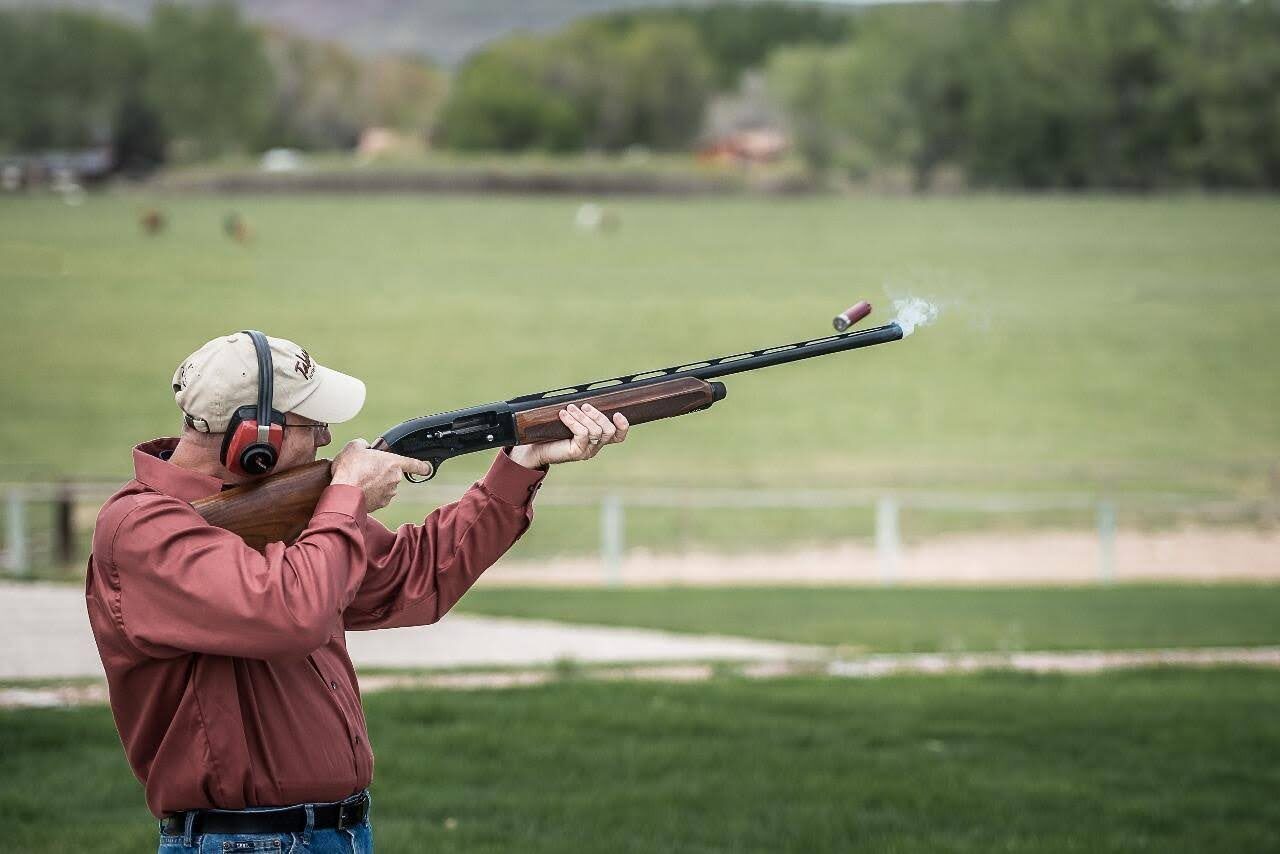 A person aiming a shotgun outdoors.