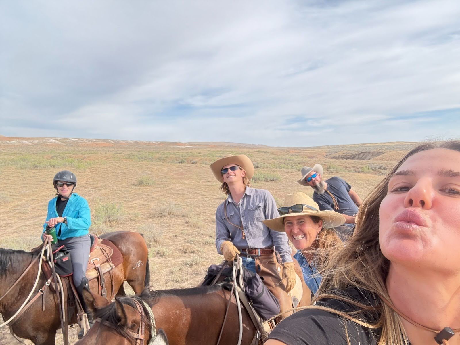 A close-up group photograph with horseback riders on open grassland.