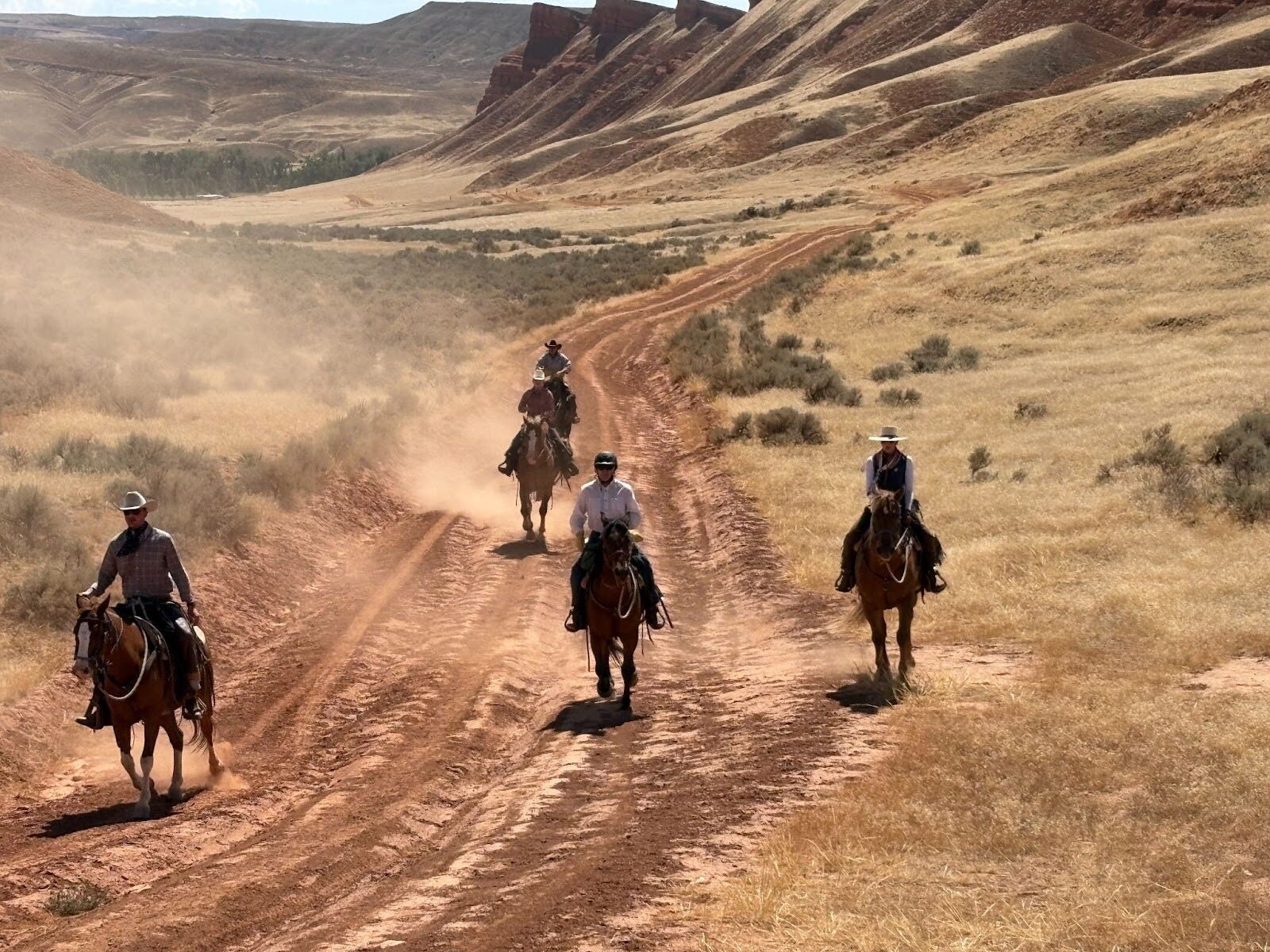 A group of horseback riders following a dusty trail through rolling hills.
