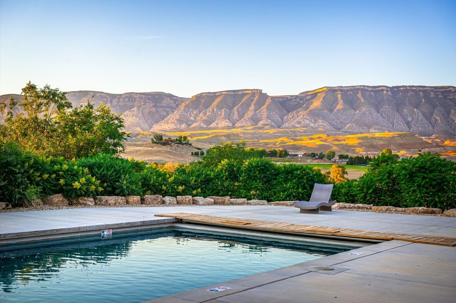 Outdoor swimming pool with trees and a rocky mountain ridge beyond.
