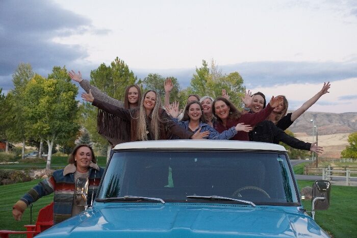 A group smiling and waving around a blue pickup truck.