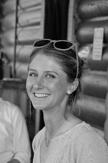 Black-and-white portrait of a smiling woman beside a log wall.