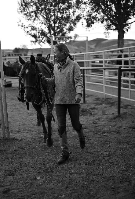 Black-and-white photograph of a person leading a dark horse near a fence.