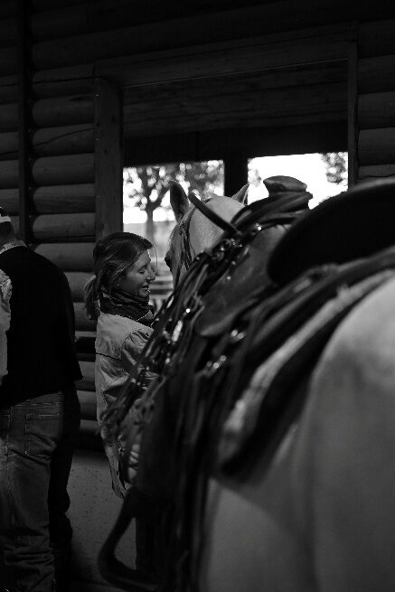 Black-and-white view of a saddled horse beside a log building.