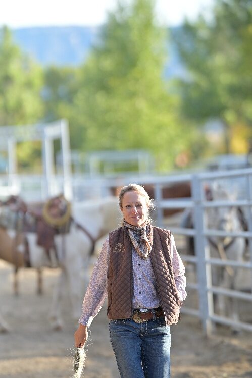 A person walking beside a white fence with horses behind it.