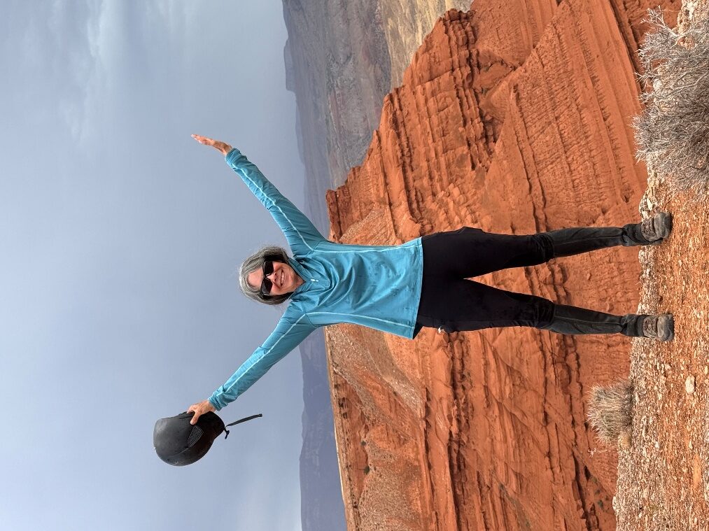 A person standing with arms outstretched against red sandstone hills.