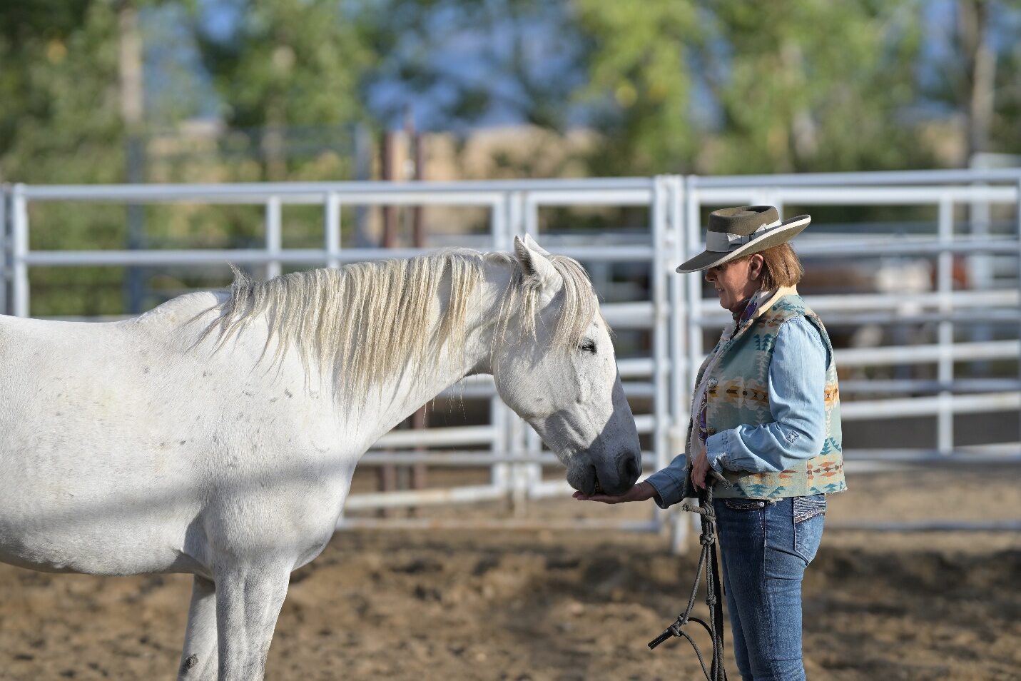 A person holding the lead of a gray horse beside a white fence.