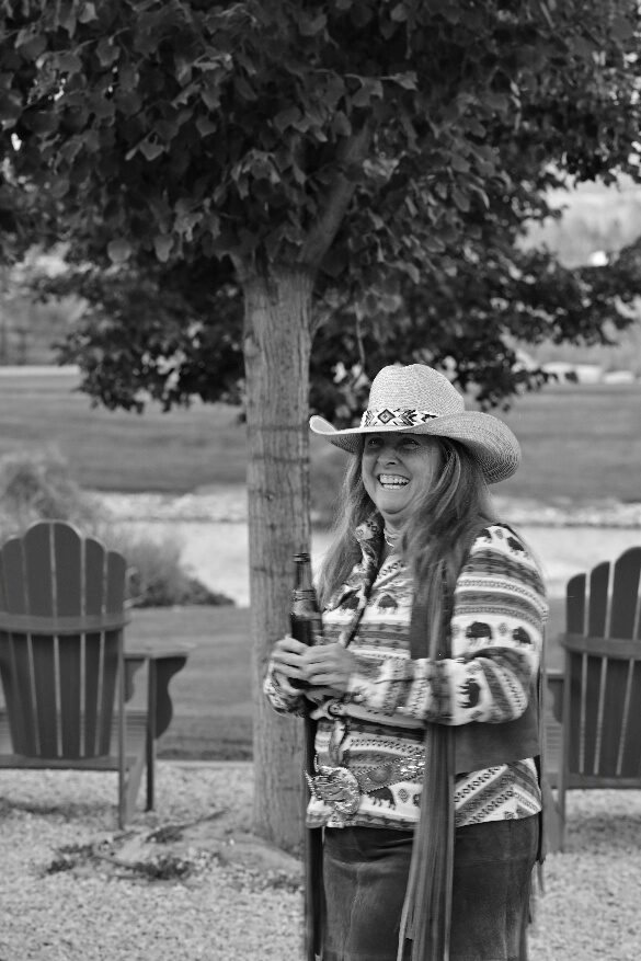 Black-and-white portrait of a person in a cowboy hat beside a tree.